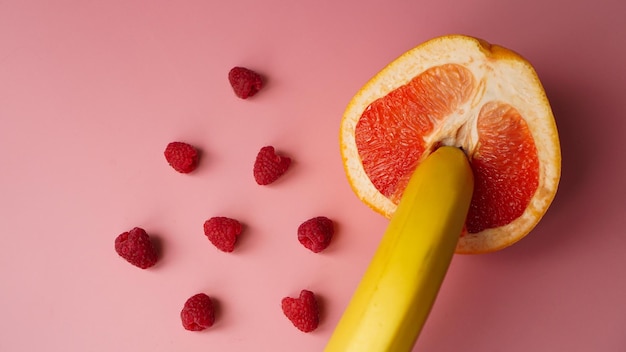 Банан с красным грейпфрутом и малиной на розовом фоне, секс-концепция