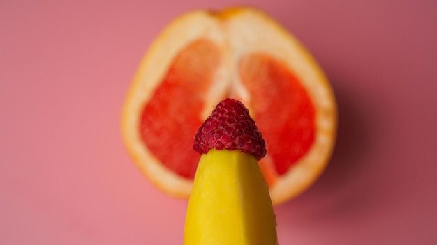 Банан с красным грейпфрутом и малиной на розовом фоне, секс-концепция