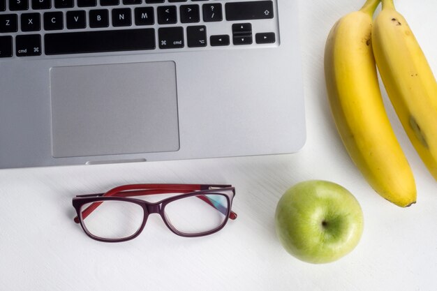 Bananas and apple near laptop and glasses