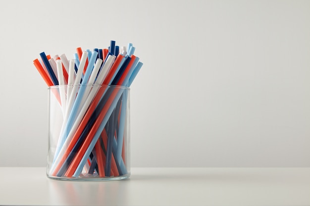 Free photo banch of pastel vivid colored thick drinking straw in transparent glass pot isolated on white table