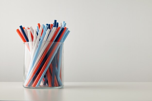 Banch of pastel vivid colored thick drinking straw in transparent glass pot isolated on white table