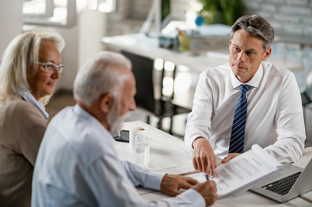 Free photo bank manager having a meeting with senior couple and pointing at place they need to sign on the contract