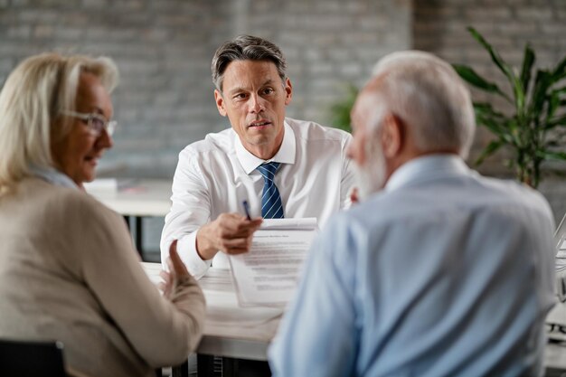 Bank manager showing to a senior couple terms of loan contract while having a meeting in the office