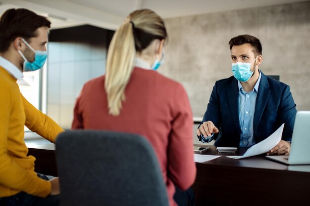 Bank manager talking to a couple and wearing protective face mask during the meeting