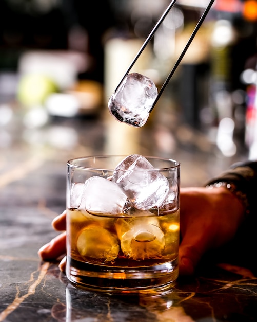 Bar tender adds ice with steel clip into cocktail glass