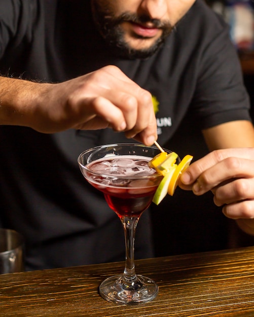 Bar tender decorated cocktail glass with fruit pieces on bamboo skewer