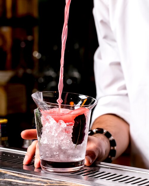 バーテンダーがグラスに氷を入れたグラスにピンクのカクテルを注ぐ