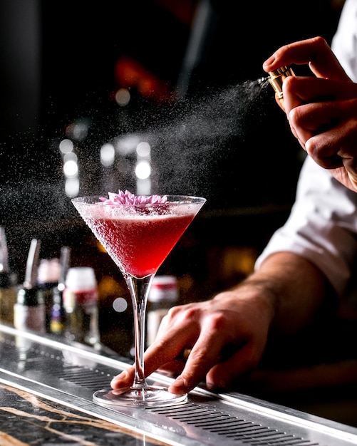 Bar tender sprays on cocktail glass garnished with flower