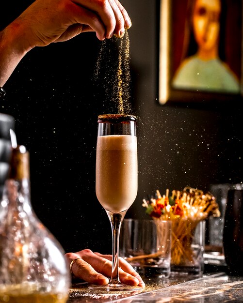 Bar tender sprinkles golden glitter into cocktail in champagne glass