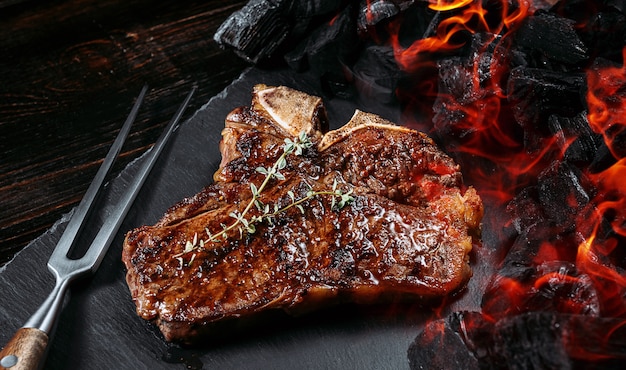 Barbeque steak on a black slate board with meat fork and grill coals