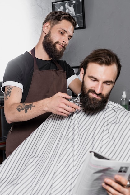Barber cutting male customer's beard with scissors