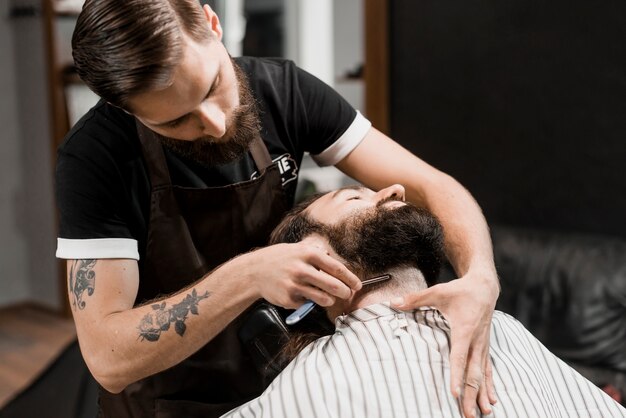 Barber cutting man's beard with razor