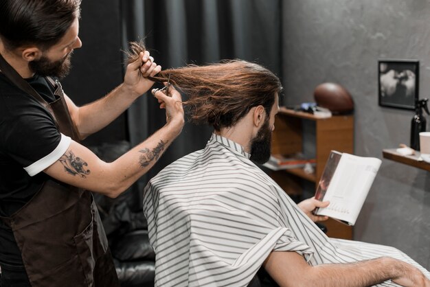 Foto gratuita barbiere che taglia i capelli lunghi nel negozio di barbiere