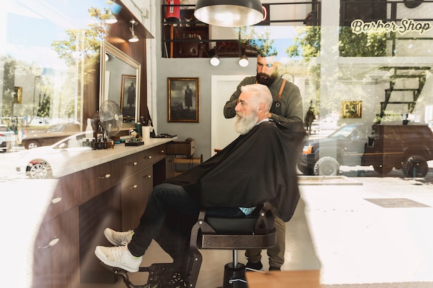 Barber doing haircut bearded aged client in hair salon