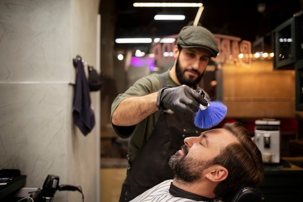 Foto gratuita barbiere che spolvera i capelli del suo cliente dalla sua faccia