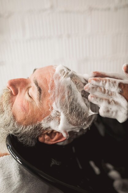 Barber hands and old male client shampooed head