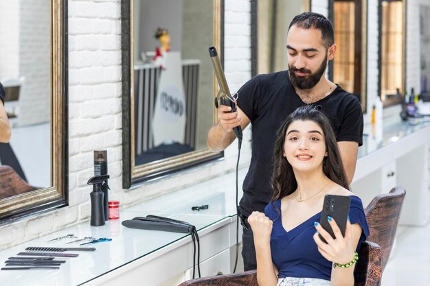 A barber holding had dryer and his client squeezing her fist and holding phone High quality photo