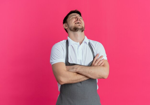 barber man in apron bothered and tired with arms crossed standing over pink wall
