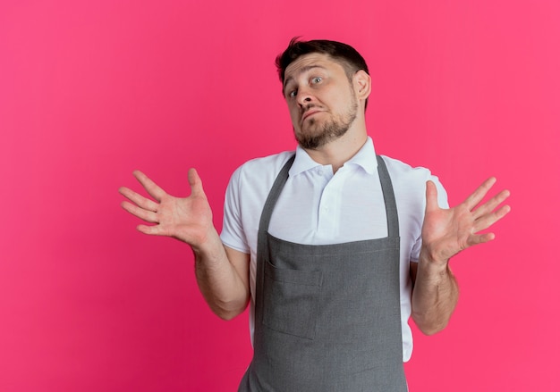 Free photo barber man in apron  confused and uncertain shrugging shoulders standing over pink wall