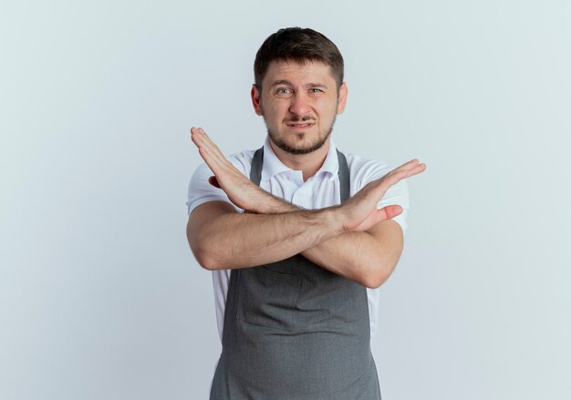 Barber man in apron displeased showing stop sign crossing hands standing over white wall