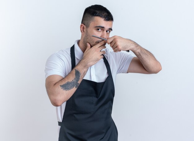 Barber man in apron going to shave holding razor looking confident standing over white