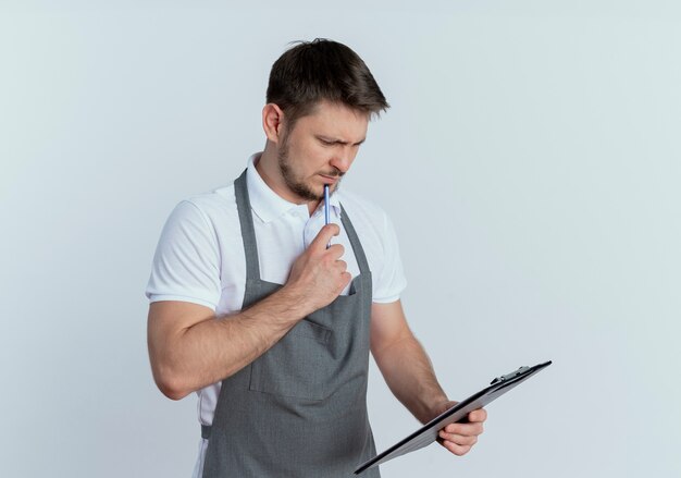 白い壁の上に立っている顔に物思いにふける表情でクリップボードを保持しているエプロンの床屋の男