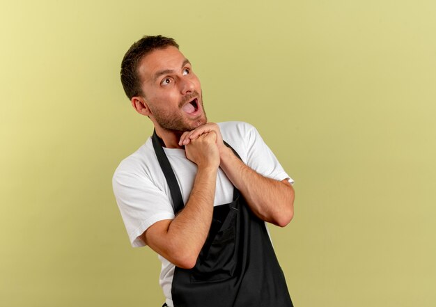 明るい壁の上に立って驚いて驚いたエプロンの床屋の男