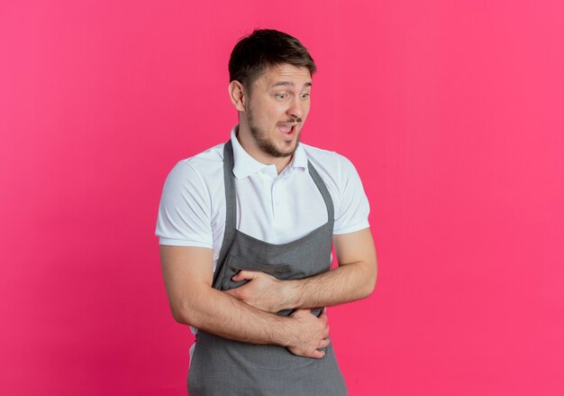 Barber man in apron looking aside with happy face laughing out standing over pink background