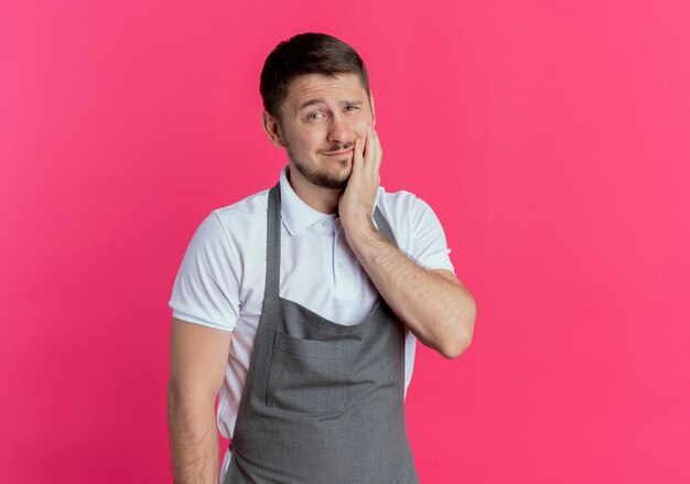 Barber man in apron looking at camera looking at camera confused and very anxious standing over pink background