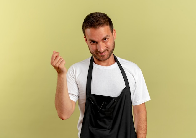 Free photo barber man in apron looking to the front rubbing fingers asking for money standing over light wall