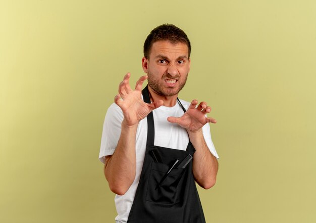 Barber man in apron making defense gesture with hands with disgusted expression standing over light wall