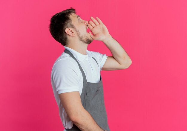 парикмахер в фартуке кричит или зовет кого-то рукой у рта, стоящего над розовой стеной