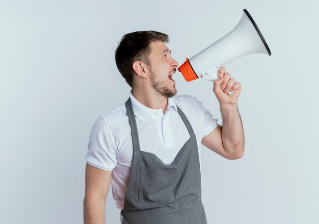 Barber man in apron shouting to megaphone standing over white background