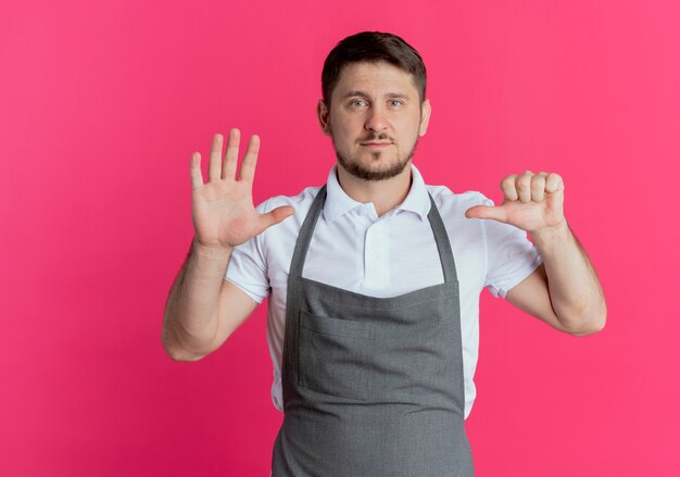 앞치마에 이발사 남자가 표시되고 분홍색 배경 위에 자신감이 서있는 6 번 손가락으로 가리키는