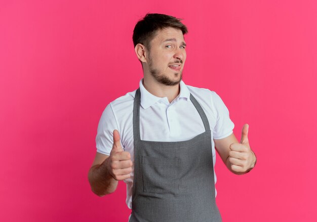barber man in apron  smiling showing thumbs up standing over pink wall