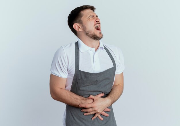 Barber man in apron touching his belly looking unwell suffering from pain standing over white background
