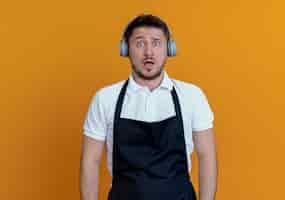 Free photo barber man in apron with headphones looking at camera confused and very anxious standing over orange background