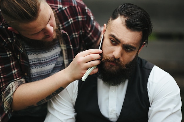 Barber shaves a bearded man in vintage atmosphere