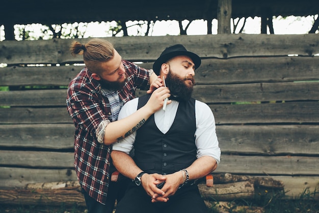 Barber shaves a bearded man in vintage atmosphere