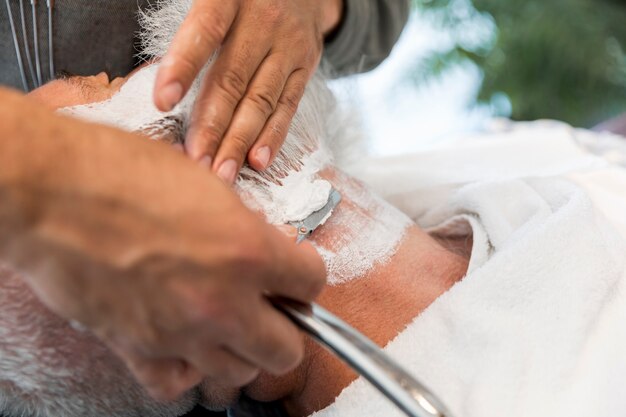 Barber shaving beard to man in salon