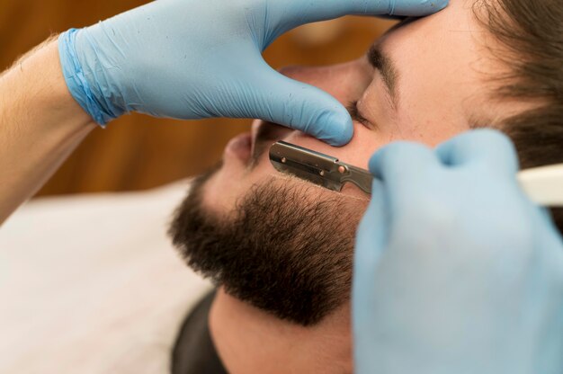 Barber shaving and contouring male customer's beard