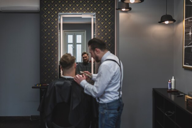 Парикмахерская бритья волос клиента рядом с зеркалом