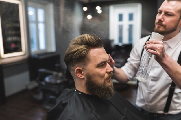 Barber spraying hair of man