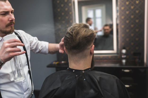 Barbiere che spruzza i capelli di un cliente irriconoscibile