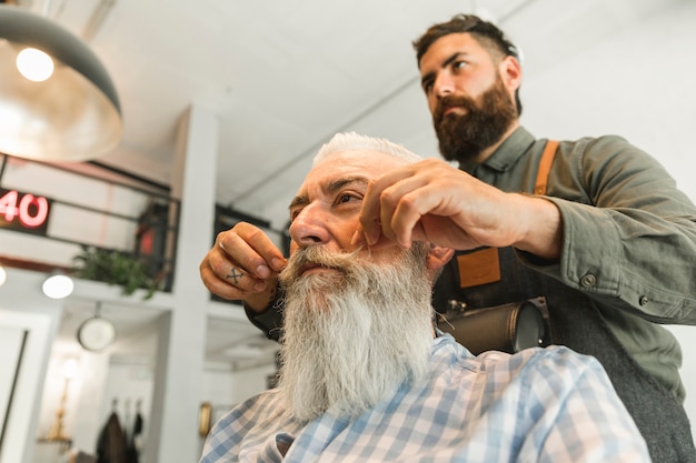 Foto gratuita barbiere raddrizzare i baffi del cliente anziano