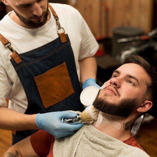 Barber using shaving cream to contour male customer's beard