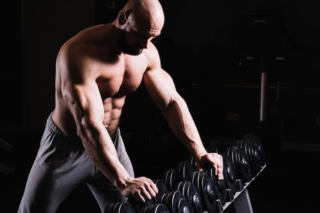 Bare-chested man leaning on dumbbells