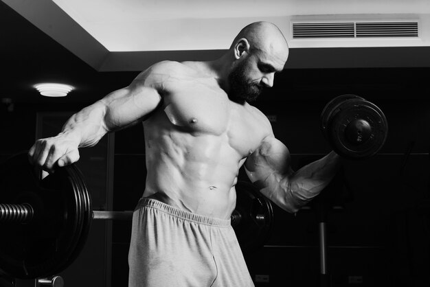 Bare-chested man lifting dumbbell near barbell