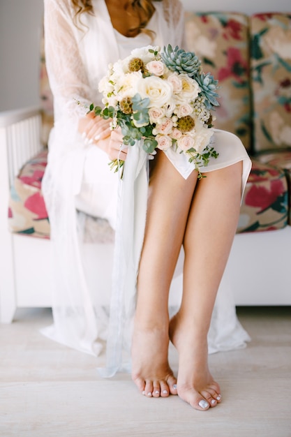 Barefoot bride in a lace robe sits ...