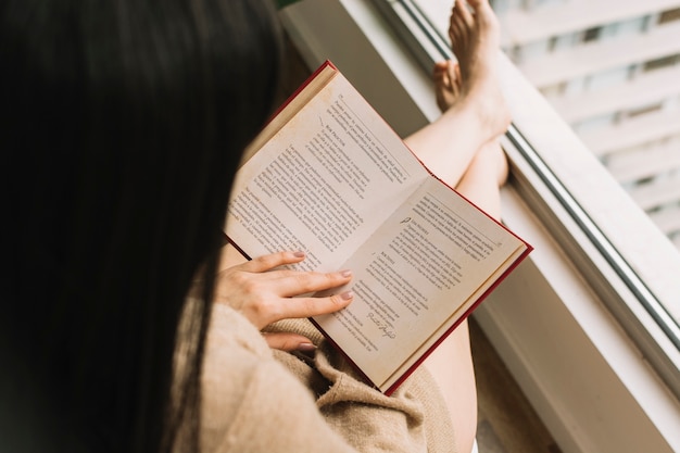 Free photo barefoot female reading near window